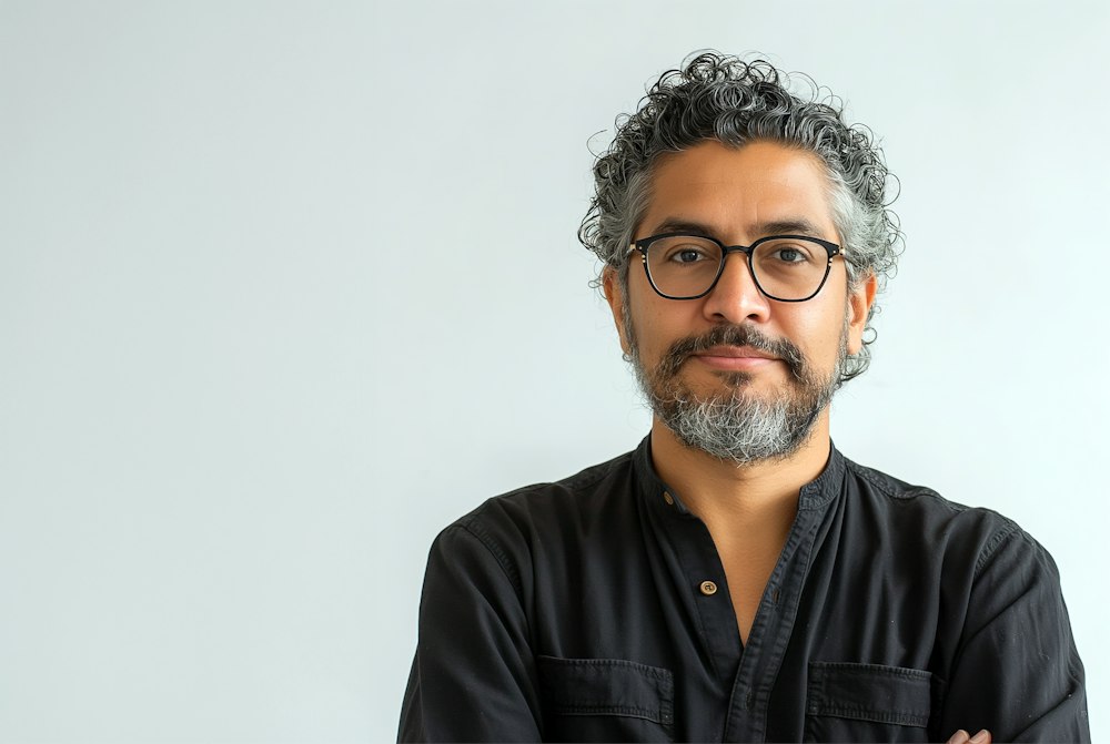 Portrait of Ruben Janssen, a man with curly grey hair, glasses and a beard in a black shirt