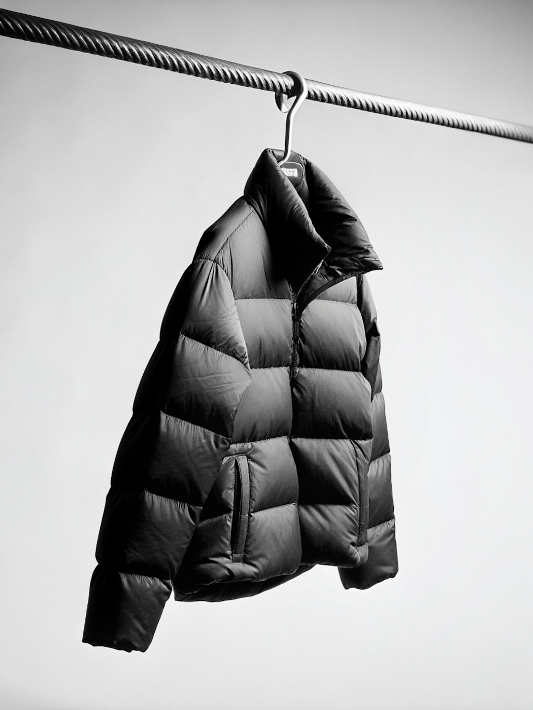 Black quilted puffer jacket hanging from a steel cable rail, photographed in black and white